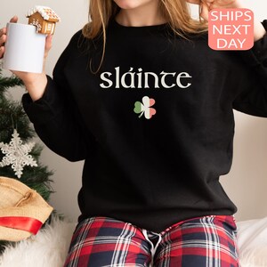 May include: Black sweatshirt with the Irish phrase "sl&aacute;inte" and a green shamrock with red and white accents.