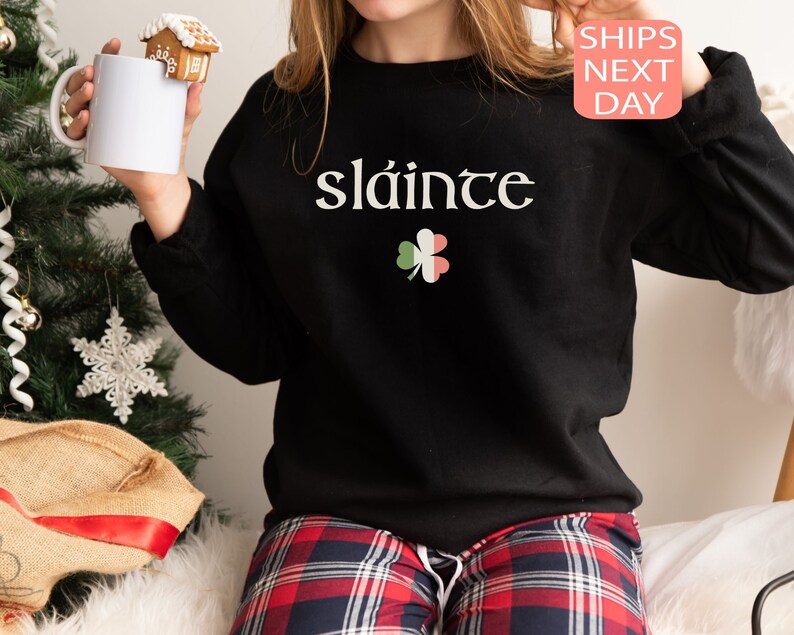 May include: Black sweatshirt with the Irish phrase "sl&aacute;inte" and a green shamrock with red and white accents.