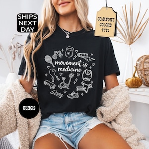 K&ouml;nnte beinhalten: Schwarzes T-Shirt mit wei&szlig;en Strichzeichnungen von Fitnessger&auml;ten und dem Schriftzug "movement is medicine". Das Shirt hat ein Etikett mit der Aufschrift "Comfort Colors 1717". Ein schwarzer Kreis mit dem Wort "BLACK" ist ebenfalls sichtbar.