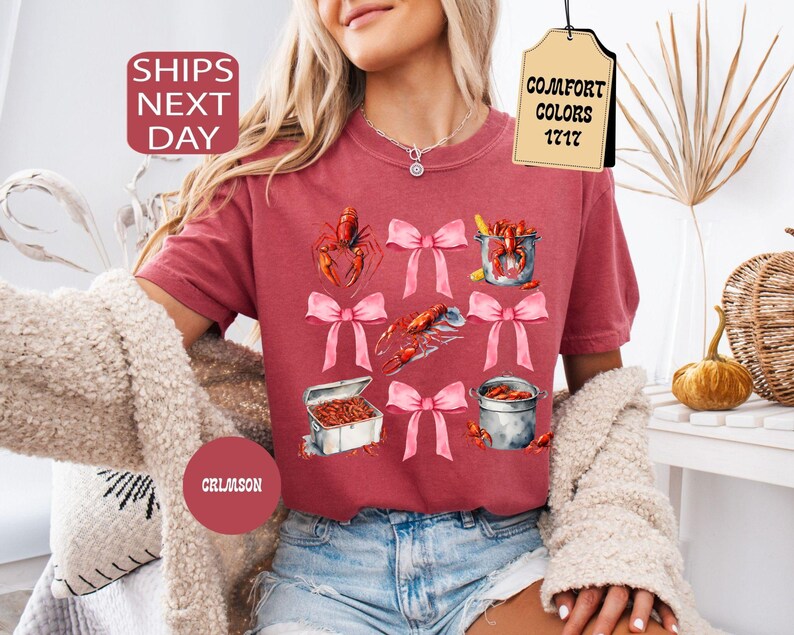 K&ouml;nnte beinhalten: Ein T-Shirt in kirschroter Farbe mit einem grafischen Aufdruck von Krebsen, rosafarbenen Schleifen und dem Text "COMFORT COLORS 1717".