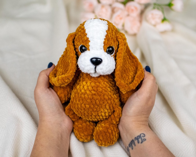 May include: A handmade plush dog toy with a brown body, long floppy ears, and a white patch on its head. The dog has a white muzzle and black eyes. The toy is soft and cuddly, perfect for children or as a decorative item.