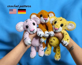 May include: Three crocheted tiger plushies in pink, orange, and yellow. The plushies are being held by a person's hands. The plushies have black stripes and white accents.