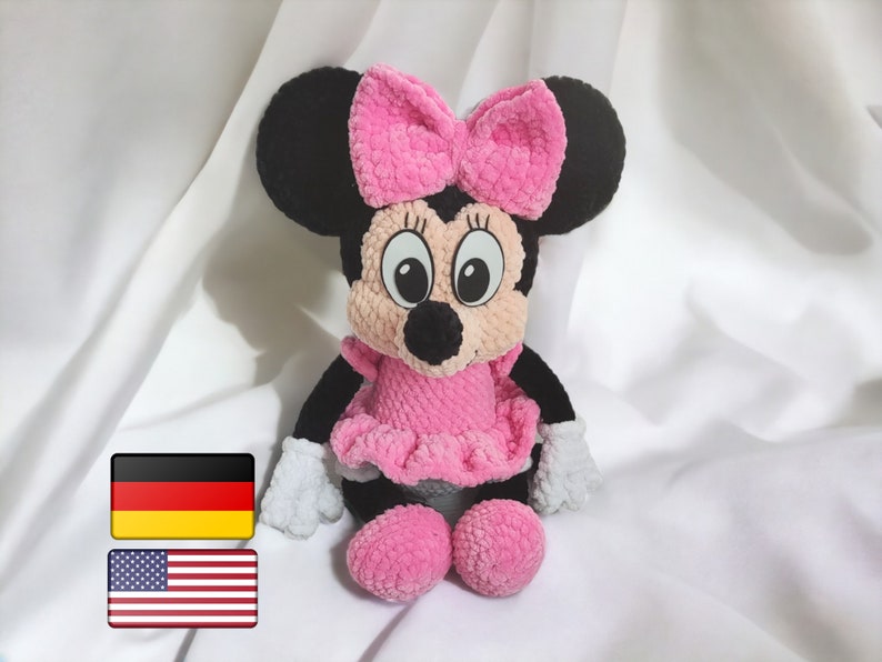 May include: A handmade plush toy of a cartoon mouse character. The toy has black ears, a pink bow, a pink dress, and pink shoes. The mouse has white gloves and a black nose. The toy is sitting on a white surface.