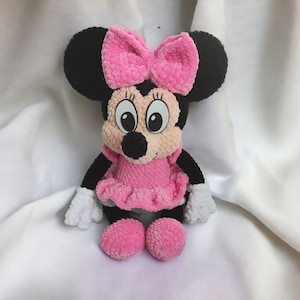 May include: A handmade plush toy of a cartoon mouse character. The mouse has black ears, a pink bow, a pink dress, and white gloves. The toy is made of soft, textured yarn and has large, expressive eyes.