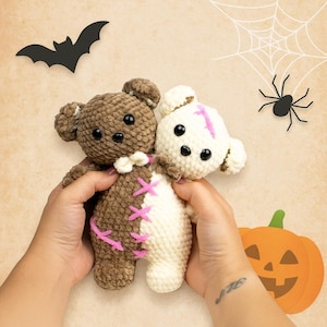 Pode incluir: Dois ursinhos de pelúcia de crochê feitos à mão, um marrom e outro creme, unidos. O urso marrom tem costuras rosa e o urso creme tem uma listra rosa. Decorações de Halloween: morcego, aranha, teia e abóbora.