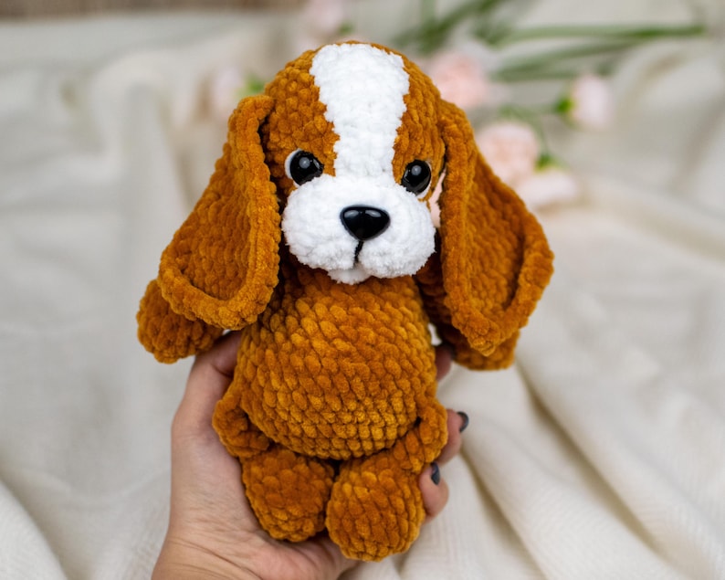 May include: A handmade plush dog toy with brown and white fur. The dog has large, floppy ears, a white muzzle, and black eyes. The toy is made of a soft, textured material and is designed to resemble a beagle puppy.