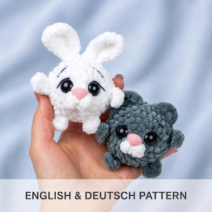 May include: Two small crocheted plush toys, one white rabbit and one dark gray cat, both featuring large black plastic eyes, pink noses, and textured yarn construction. The text at the bottom of the image reads ENGLISH & DEUTSCH PATTERN.