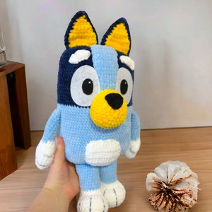 May include: A blue and yellow crocheted stuffed dog toy with white accents. The dog has large black eyes and a black nose.