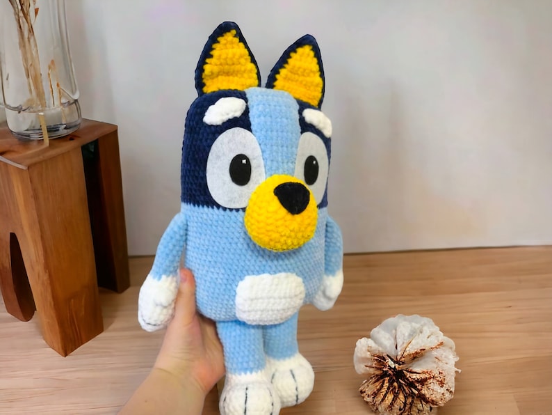 May include: A blue and yellow crocheted stuffed dog toy with white accents. The dog has large black eyes and a black nose.