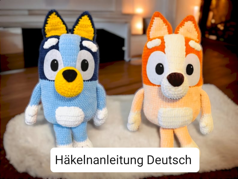 May include: Two crocheted stuffed dog toys, one blue and one orange, with white accents. The toys are sitting on a white fluffy surface. The text "H&auml;kelanleitung Deutsch" is visible at the bottom of the image.