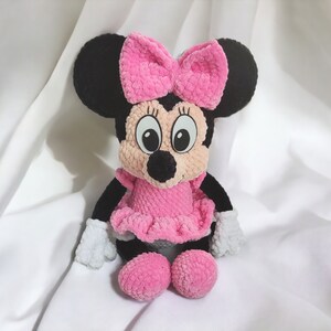 May include: A handmade plush toy of a cartoon mouse character. The toy has black ears, a pink bow, a pink dress, and pink shoes. The mouse has white gloves and a smiling face with large eyes.