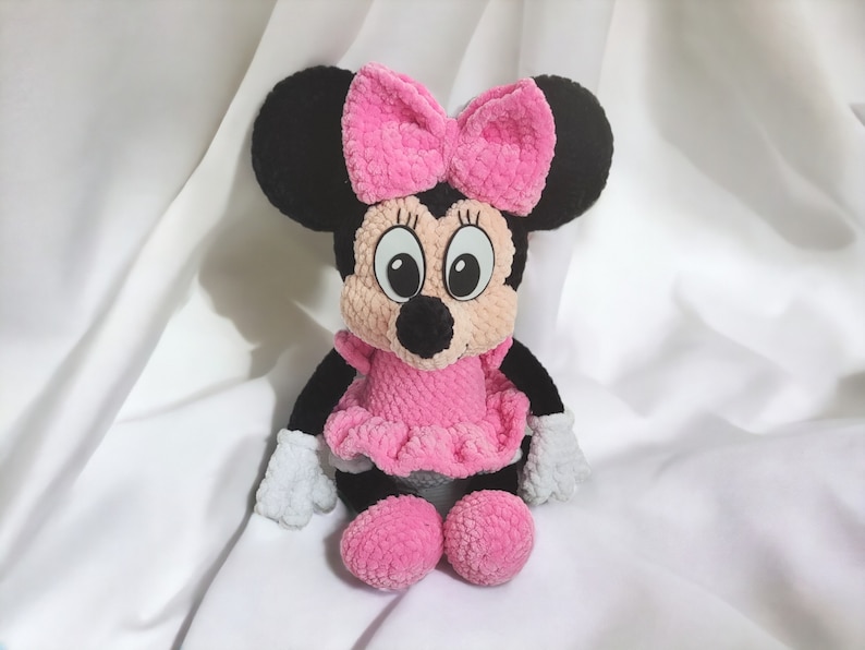 May include: A handmade plush toy of a cartoon mouse character. The toy has black ears, a pink bow, a pink dress, and pink shoes. The mouse has white gloves and a smiling face with large eyes.