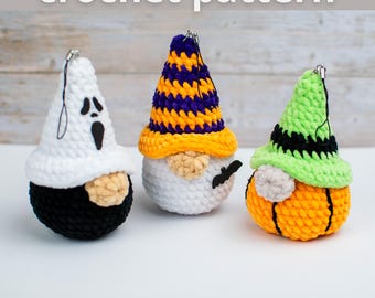 May include: Three handmade crochet Halloween gnome ornaments. One is a ghost, one is a wizard, and one is a pumpkin. The ghost is white with a black face and black body. The wizard has a purple and yellow hat. The pumpkin has a green hat.