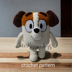 May include: Crochet pattern for a white, brown and orange dog plush toy. The toy has big eyes and a black nose. The toy is standing on a wooden surface. "Cute Happy Toys" is written on the surface.