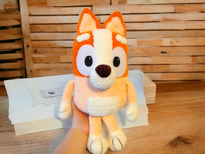 May include: A crocheted stuffed dog toy with orange, white, and brown fur. The dog has large, black eyes and a brown nose.