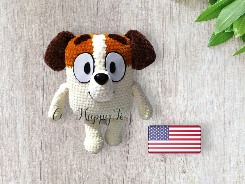 May include: A crocheted stuffed dog toy with brown ears, white fur, and orange and brown spots. The dog has large white eyes and a black nose.