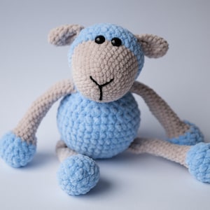 May include: A blue and beige crocheted stuffed sheep toy. The sheep has a light blue body, beige face, and black eyes.