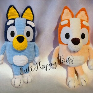 May include: Two crocheted stuffed dog toys. The blue dog has yellow ears and a yellow nose. The orange dog has white ears and a brown nose. Both dogs have big eyes and are sitting on a white surface. "Cute Happy Toys" is written in white text on the surface.