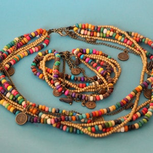 May include: A multi-strand necklace and bracelet set. The necklace and bracelet feature colorful wooden beads in various colors, including red, yellow, green, and blue. Gold-colored chains and small coin charms add detail.