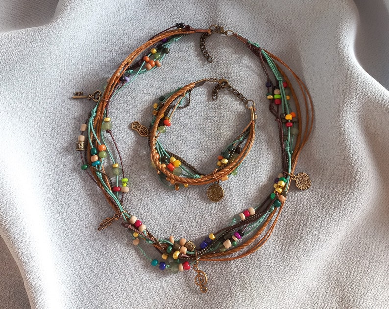 May include: A set of two beaded necklaces with brown leather cords, turquoise, green, yellow, red, and orange beads, and metal charms. The necklaces are layered and feature a key charm, a tree charm, and a circular charm.