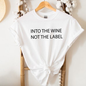May include: White t-shirt with the text "Into the wine not the label" printed in black.