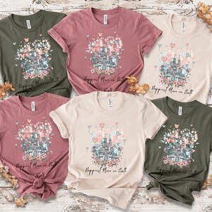 May include: A collection of six short-sleeved t-shirts in various colors, including olive green, dusty rose, and cream. Each shirt features a castle graphic with floral and heart accents, and the text "Happiest Place on Earth".