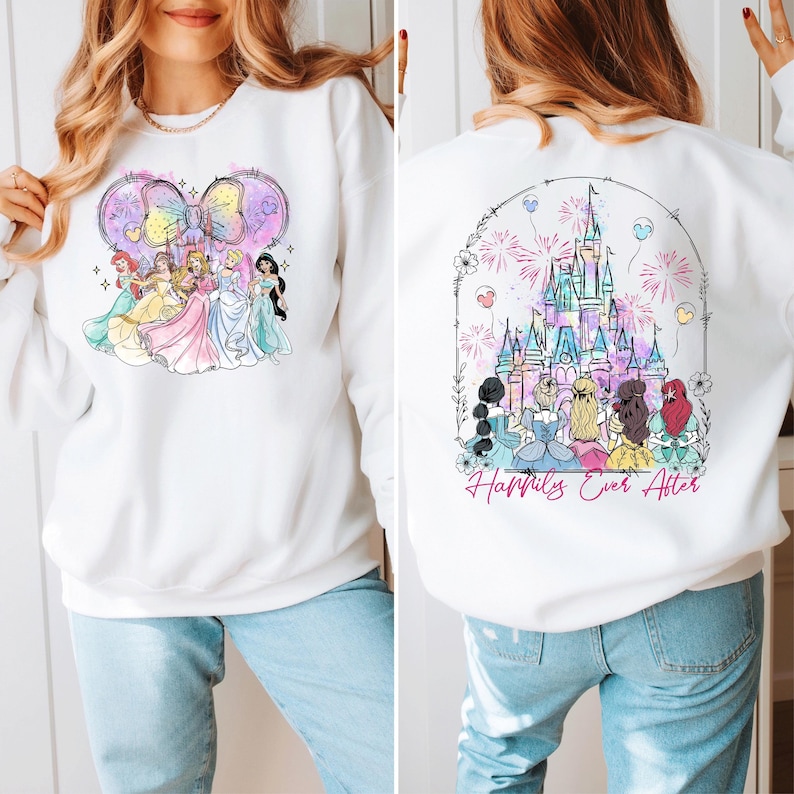 Puede incluir: Sudadera blanca con una ilustraci&oacute;n colorida de princesas Disney frente a un castillo con fuegos artificiales y el texto "Happily Ever After" en la espalda.
