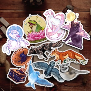 May include: A set of ten colorful stickers featuring various animals and nature scenes. The stickers include a white lamb, a black and white wolf, a red fox, a blue bird, a blue and gray owl, a gray bird, a green frog, a white ferret, a black cat, and a music box.