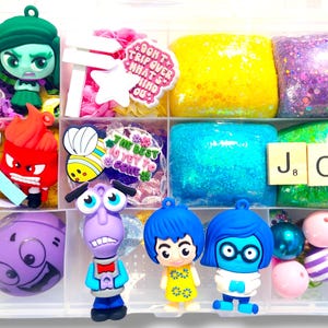 May include: A clear plastic organizer filled with colorful items. Includes character figurines, glittery blocks, and decorative elements. The word "JOY" is spelled out with letter tiles. A variety of colors are present, including yellow, blue, green, and purple.