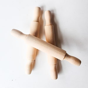 May include: Three wooden rolling pins, two are standing upright and one is lying horizontally across the other two.