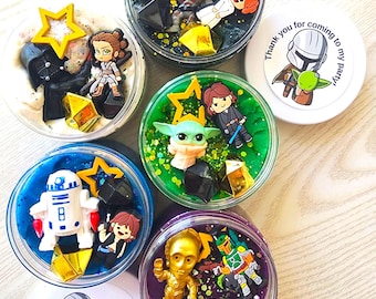 May include: A collection of sensory play jars with Star Wars-themed characters and glitter. Each jar contains a different color of sensory material and a variety of character figurines, including Darth Vader, R2-D2, and Baby Yoda. Some jars have star-shaped decorations.