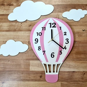 Könnte beinhalten: Rosa-weiße Heißluftballon-Uhr mit schwarzen Zeigern und Zahlen. Die Uhr ist von drei weißen Wolken umgeben.