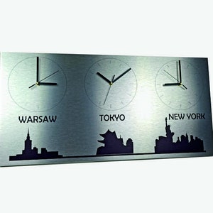 May include: A silver metal wall clock displaying three time zones: Warsaw, Tokyo, and New York. Each time zone features a black clock face with black hands and the city name printed beneath.