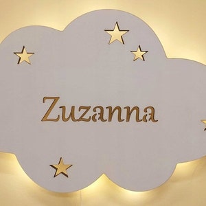 Op de afbeelding: Een wit houten wolkvormig nachtlampje met de naam "Zuzanna" uitgesneden en vijf gouden sterren.