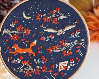 May include: Embroidered hoop art featuring a fox, owl, and other woodland creatures on a dark blue background. The design includes a crescent moon, stars, and various foliage in shades of orange, red, and white.