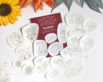 May include: A set of 16 white felt patches featuring various woodland-themed embroidery designs, including a squirrel, mushroom, hedgehog, acorn, leaves, and a heart. The patches are labelled "Woodland Stick & Stitch Embroidery Patches" and are from the brand "Tales from the Hoop."