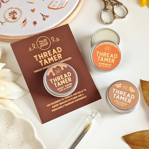 May include: Three round metal tins of Thread Tamer thread conditioner in Sticky Toffee, Pumpkin Pie, and Unscented varieties. The tins are displayed with a brown informational card featuring the text Thread Tamer and product descriptions.