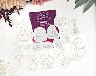 May include: A set of 12 white iron-on embroidery patches with witchy themes. The patches feature images of a cauldron, crystals, a broom, a potion bottle, a book that says "Spells", a pentagram, a candle, a witch's hat, a moon, a mushroom, a chalice, and a sprig of mistletoe. The patches are packaged on a purple card with the text "Tales from the Hoop" and "Witches Stick & Stitch Embroidery Patches".