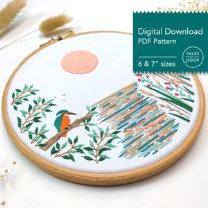 May include: Embroidered hoop art featuring a kingfisher bird perched on a branch with a sunset in the background. The hoop is 6 or 7 inches in diameter and includes a variety of colours, including green, blue, orange, and pink.