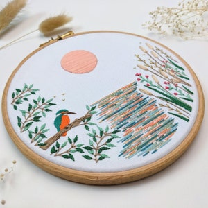 Kingfisher Lake embroidery kit. A teal green and orange kingfisher watches patiently over a peach blue orange and gold shimmering lake. An animal embroidery kit by Tales from the Hoop. A unique gift for nature, bird, craft and animal lovers.