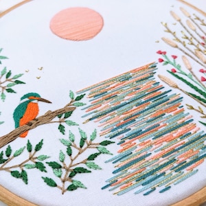 A closeup of Kingfisher Lake embroidery kit by Tales from the Hoop. A peach sun sets over a glistening lake in this magical modern full embroidery kit. For all ability levels from beginners to more experienced stitchers. A beautiful and special gift