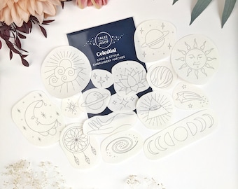 May include: A set of 14 white iron-on embroidery patches featuring celestial designs, including a crescent moon, a sun, a shooting star, a galaxy, a hand, a dreamcatcher, a lotus flower, and a planet. The patches are labelled "Celestial Stick & Stitch Embroidery Patches" and are from the brand "Tales from the Hoop."