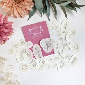 May include: A set of 15 white felt embroidery patches featuring various floral and nature-themed designs. The patches are arranged on a pink background with the text "Tales from the Hoop Wildflower Stick & Stitch Embroidery Patches" and "Lost amongst the wildflowers".