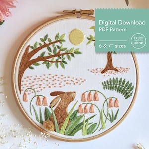 May include: Embroidered hoop art featuring a brown rabbit in a green meadow with pink flowers, a tree, and a yellow sun. The hoop is 6 or 7 inches in diameter. The text "Digital Download PDF Pattern" and "Tales from the Hoop" is in the top right corner.