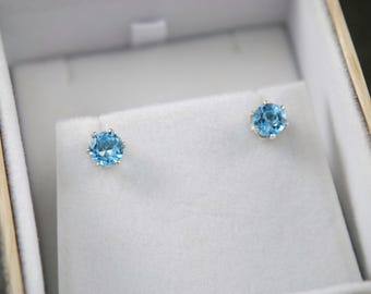 May include: A pair of silver stud earrings with round, light blue topaz gemstones.