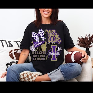 May include: Black t-shirt with a graphic design featuring the text "MISS OUR" and "Hallsville" in purple and white. The design includes a checkered bow, a Native American head, and the words "It's a good day to be an Indian."