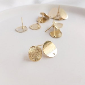 May include: A set of gold-toned metal earring blanks with a textured finish. The blanks are oval shaped with a small hole at the top for attaching earring posts.
