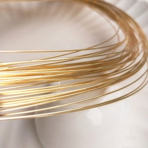 Może przedstawiać: Zbliżenie na cewkę cienkiego, błyszczącego złotego drutu. Drut jest ciasno nawinięty, tworząc okrągły kształt. Złoty kolor jest jasny i odbijający światło, sugerując materiał do wyrobu biżuterii.