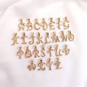 May include: A set of 26 gold-tone alphabet letter pendants with clear crystal accents. Each letter is individually crafted and features a cursive script style.