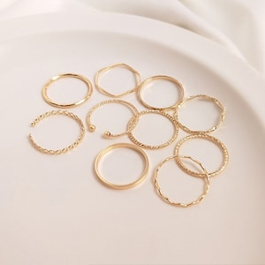 May include: Set of ten gold-toned rings with different designs, including twisted, textured, and plain bands. The rings are arranged on a white surface.